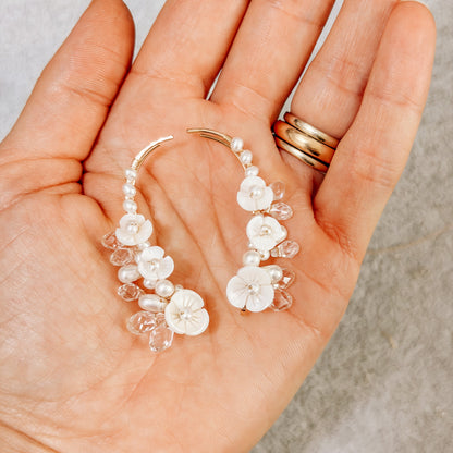 Hand holding floral pearl ear climbers to show their detailed handmade design