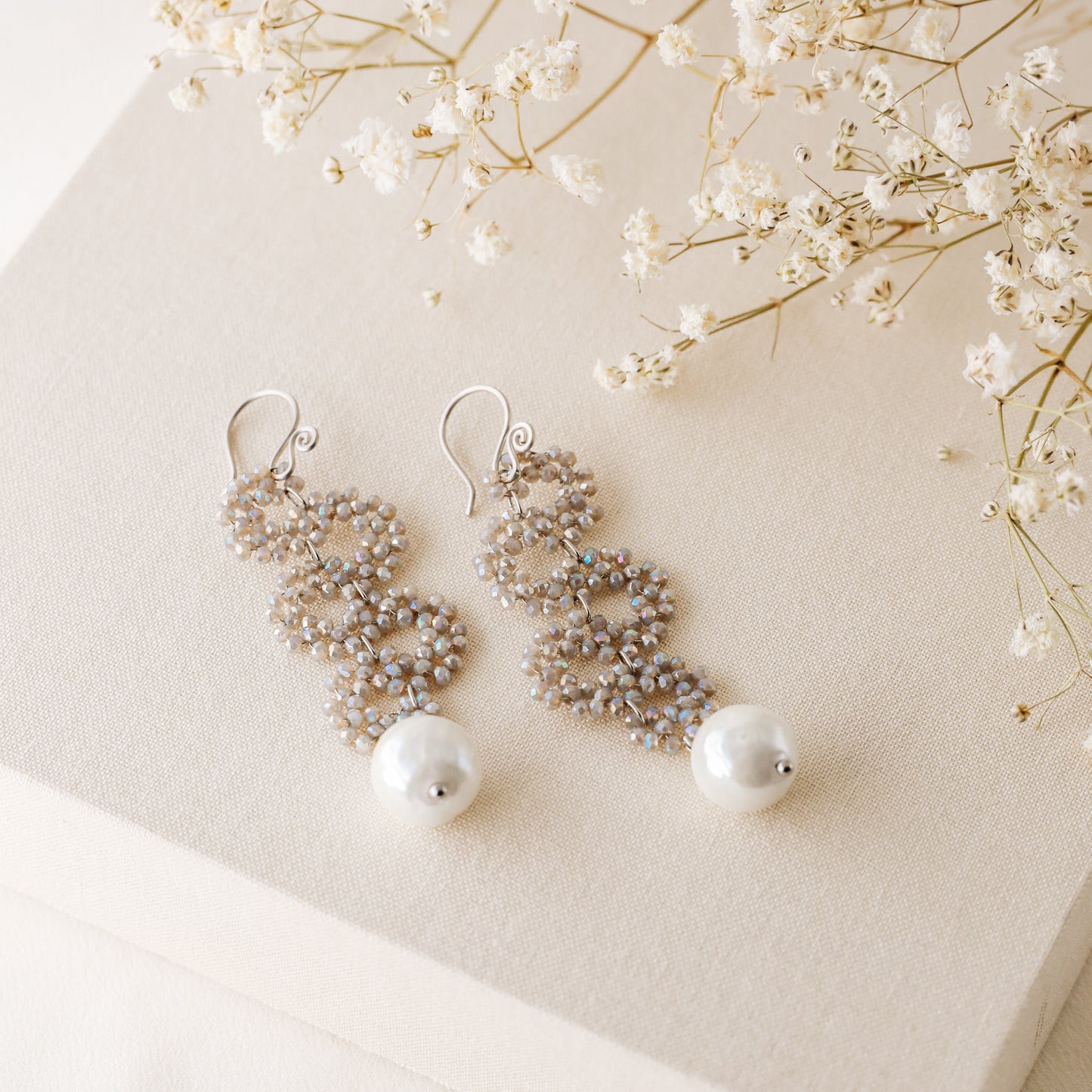 Champagne iridescent snake drop earrings with ceramic pearl on neutral fabric and flowers
