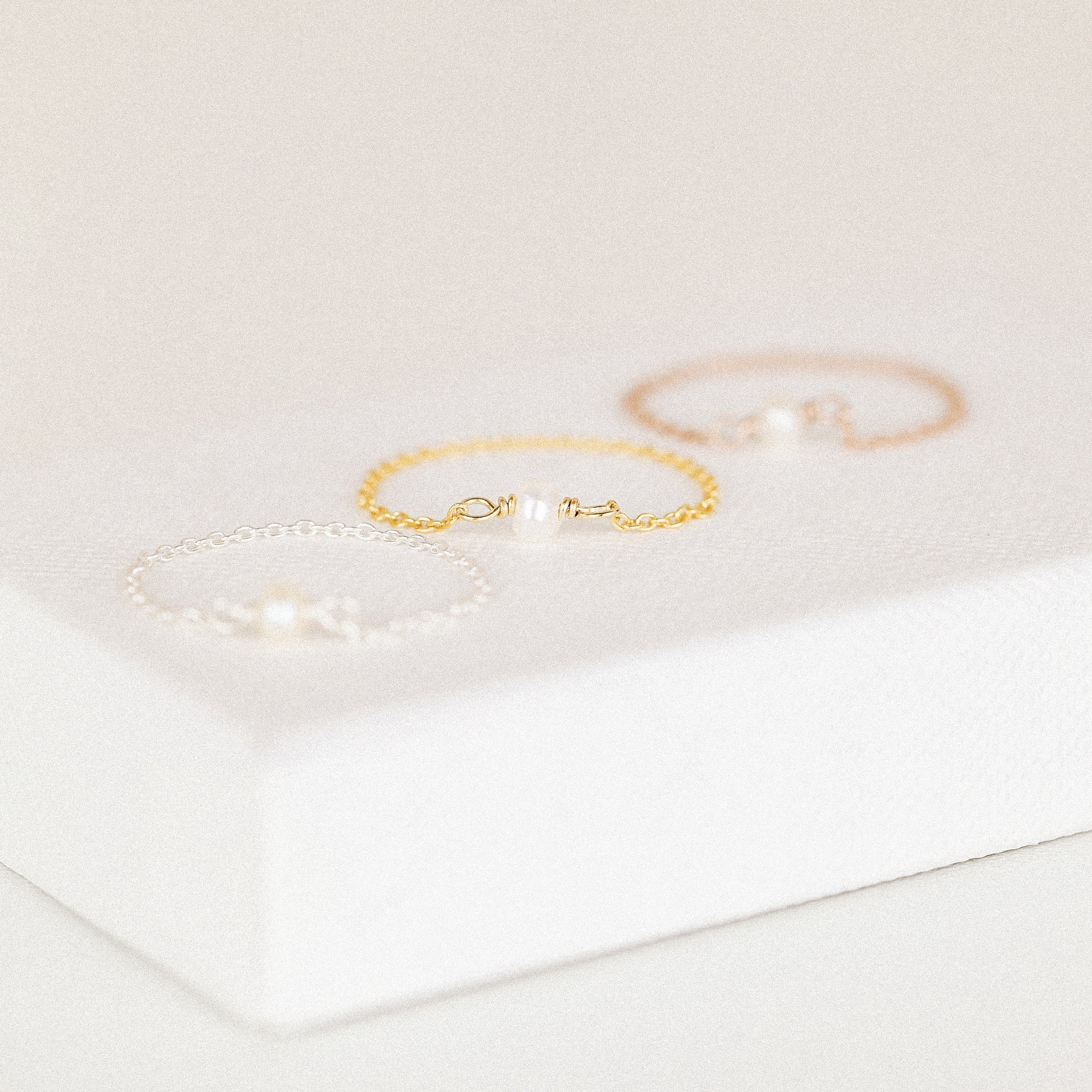 Dainty freshwater pearl chain rings in three metal colors on white jewelry display