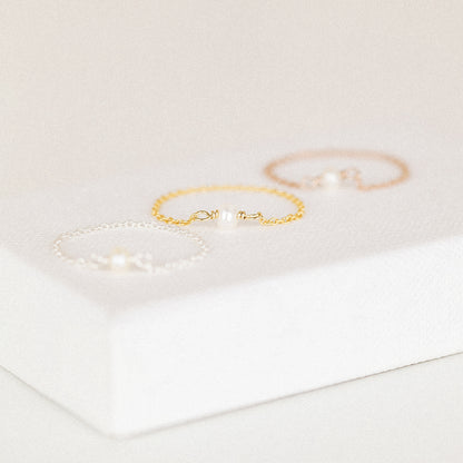 Dainty freshwater pearl chain rings in three metal colors on white jewelry display