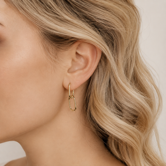 Gold double link hoop earrings worn on ear with a minimal geometric drop design