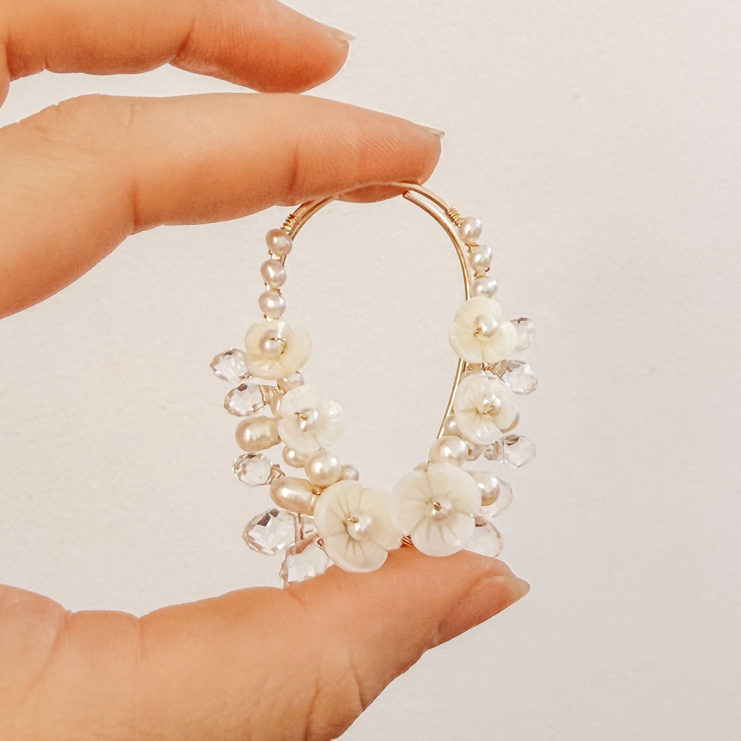 Floral crystal ear climbers held between fingers for size reference