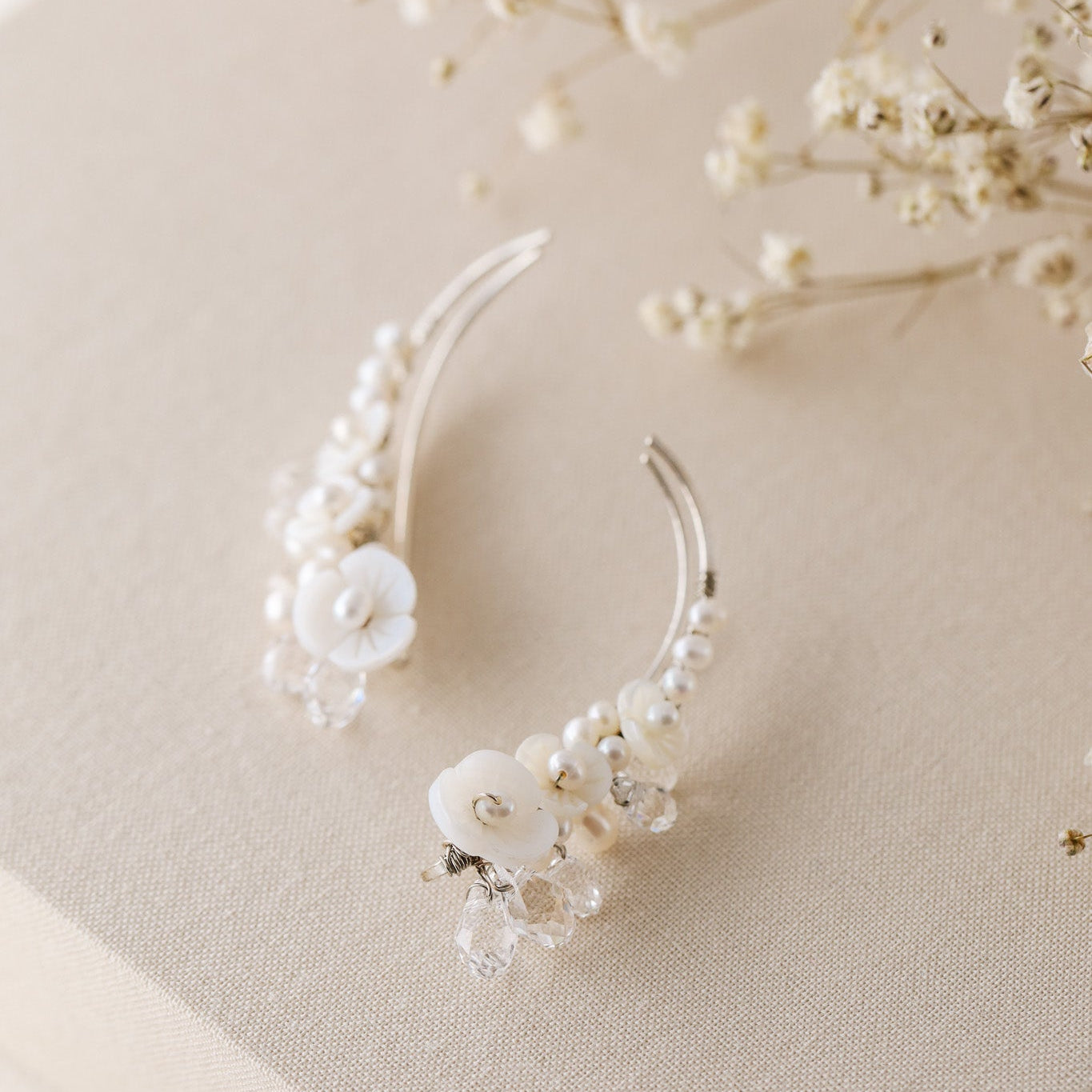 Floral crystal ear climbers held between fingers for size reference