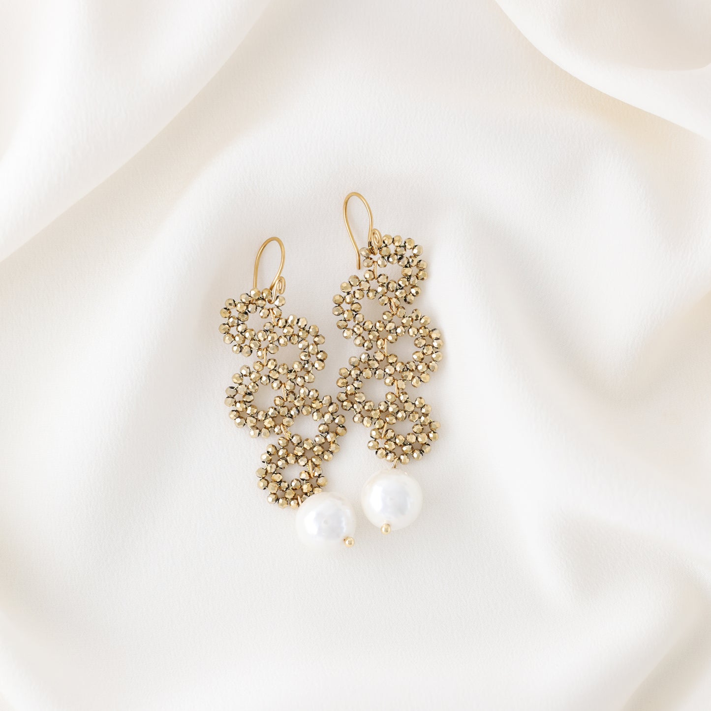 Gold beaded snake drop earrings with ceramic pearl on soft white fabric