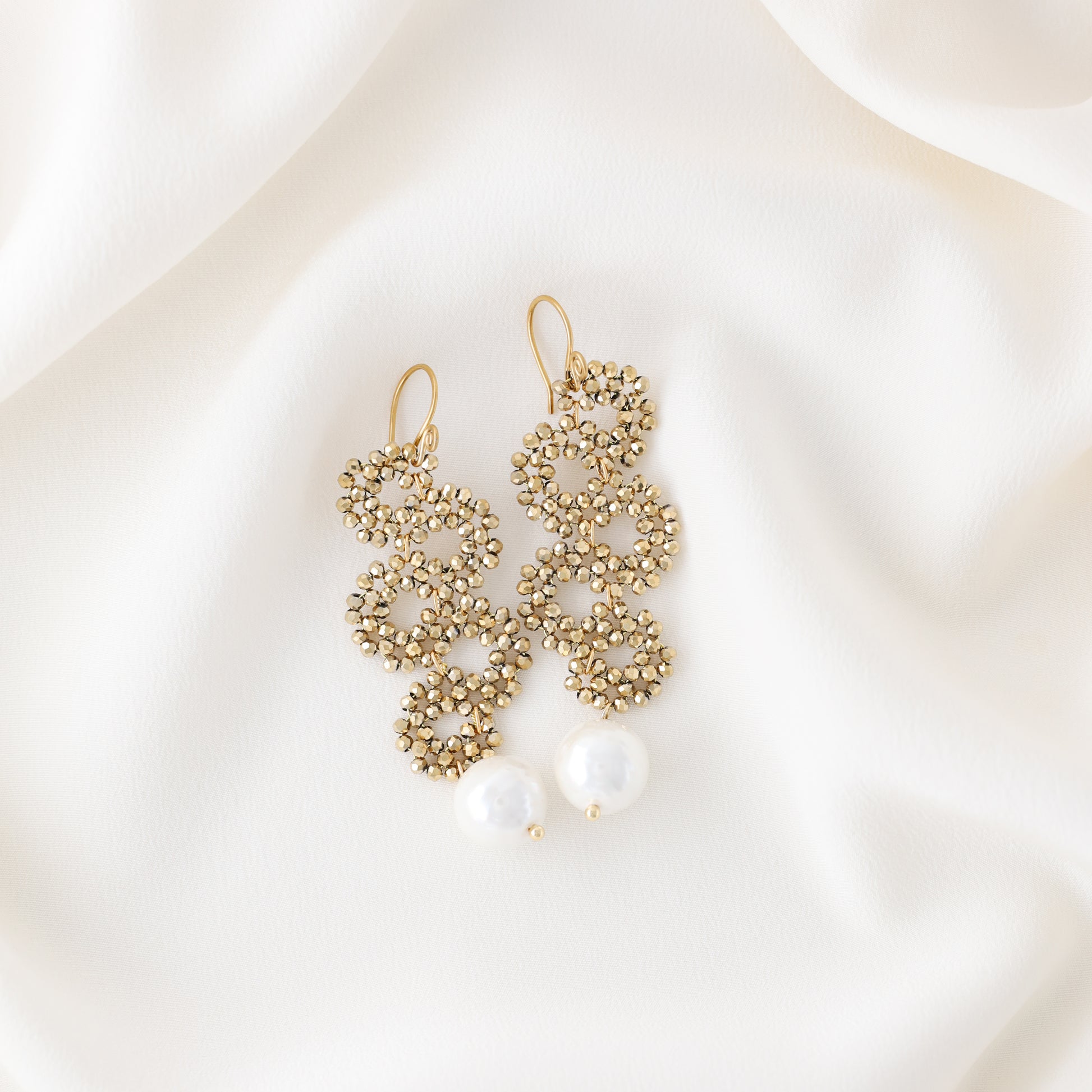 Gold beaded snake drop earrings with ceramic pearl on soft white fabric