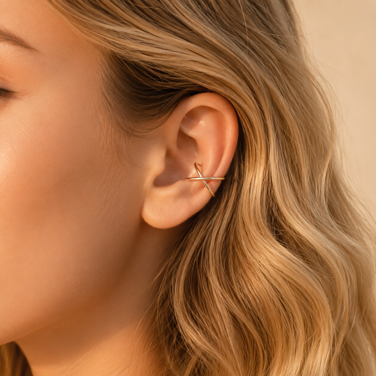 gold criss cross ear cuff worn on the upper ear, featuring a smooth minimalist no piercing design.