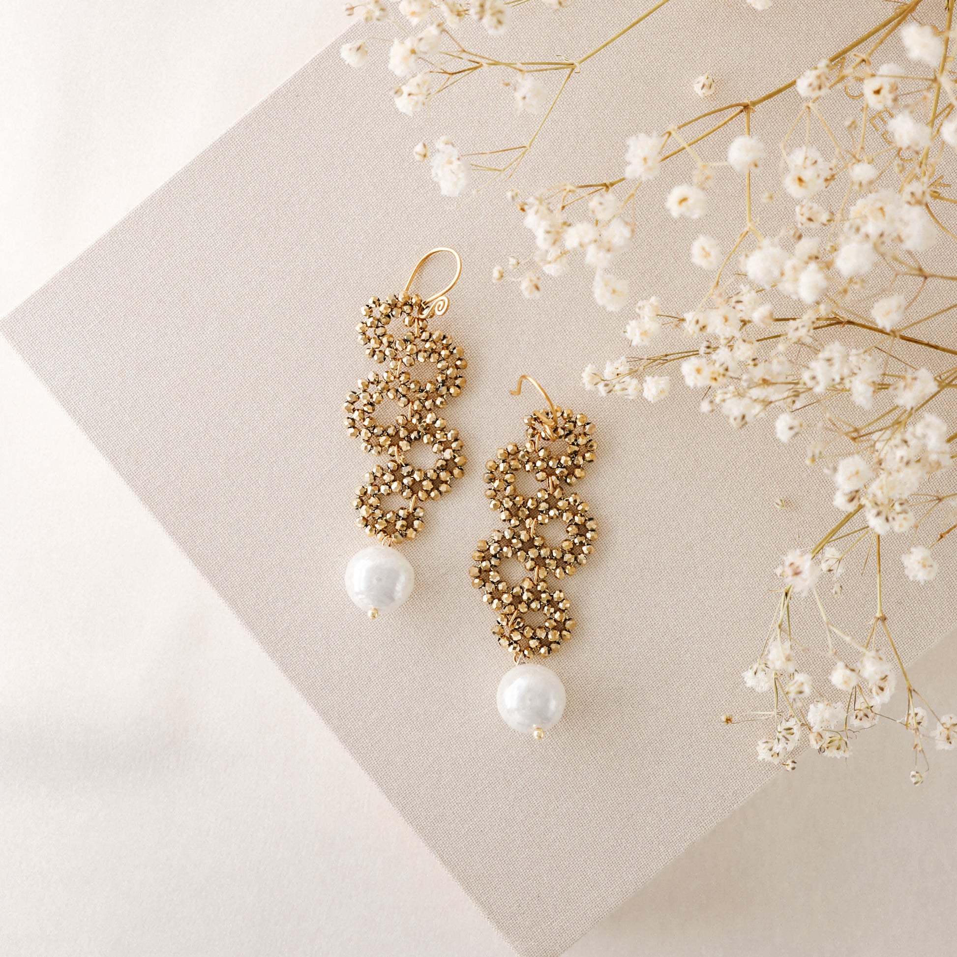 Gold crystal cascading earrings with pearl drop on neutral fabric background