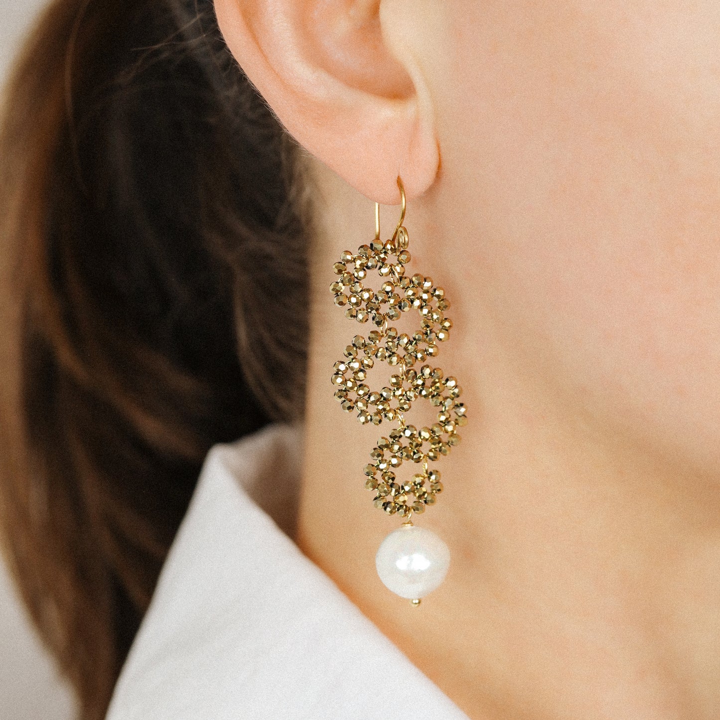 Close-up of gold crystal cascading earrings with round ceramic pearl drop