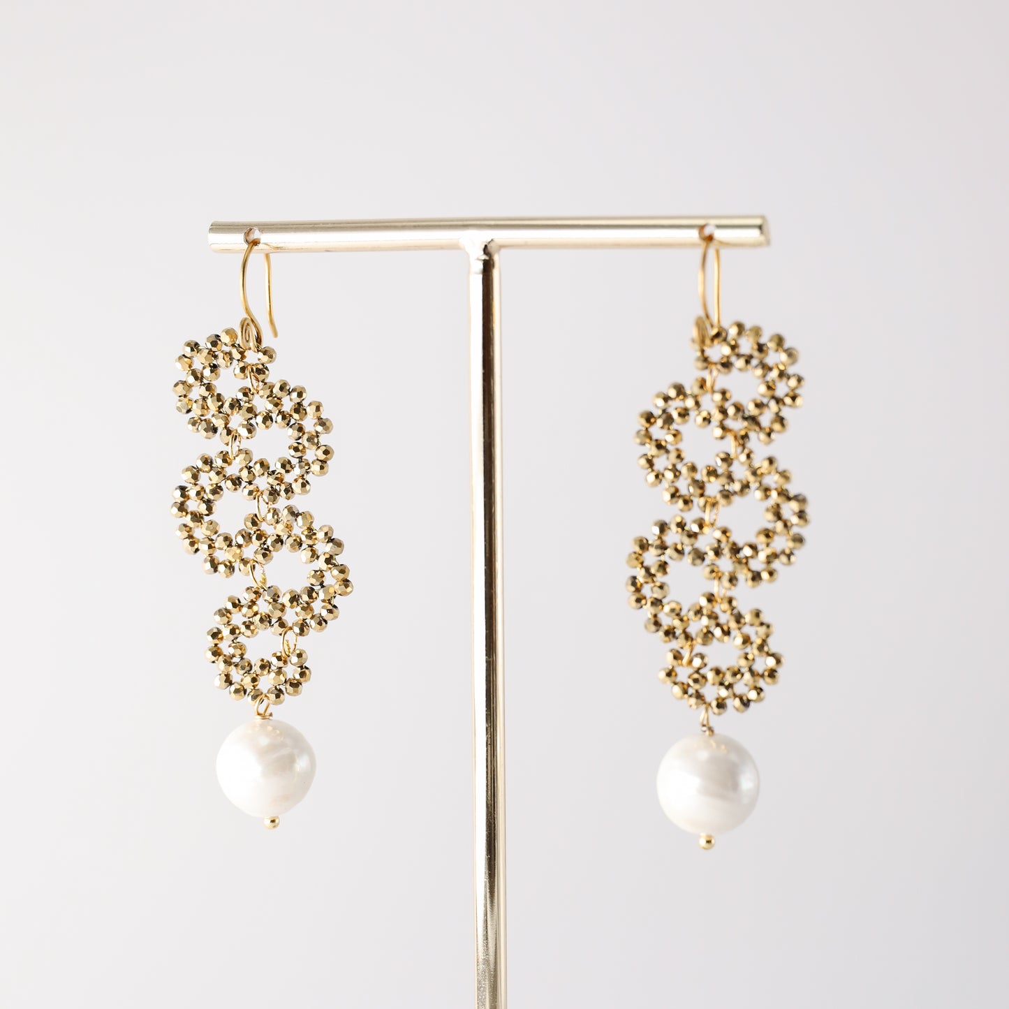 Gold crystal pearl drop earrings hanging on a jewelry display stand