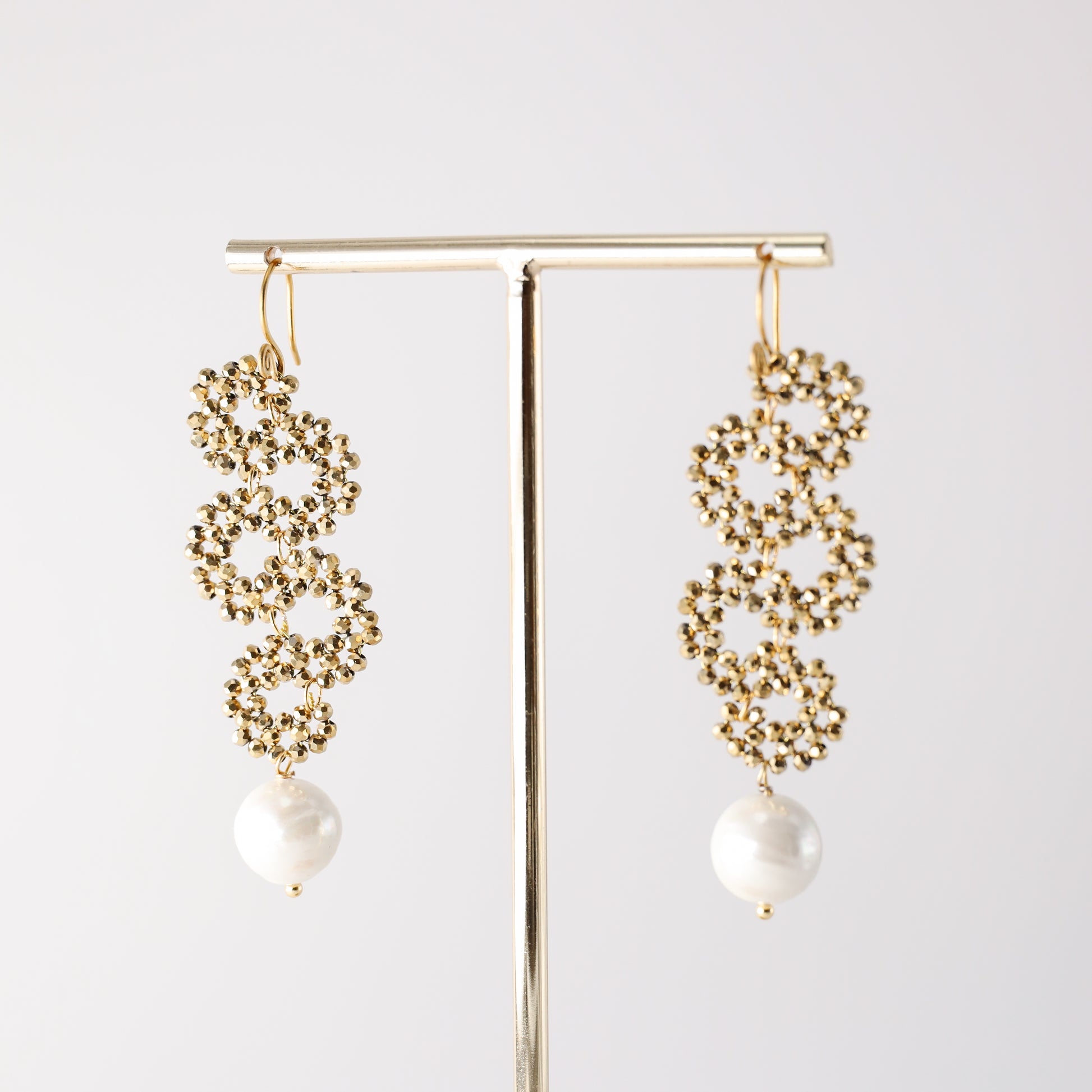 Gold crystal pearl drop earrings hanging on a jewelry display stand
