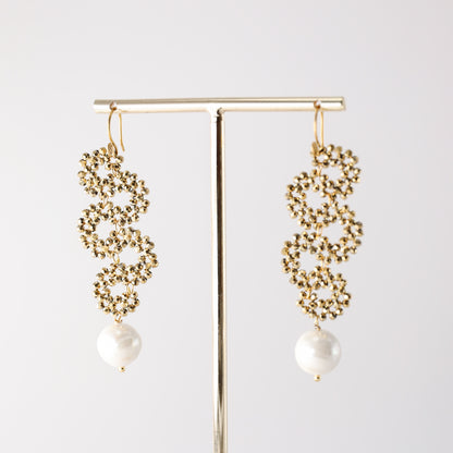 Gold crystal pearl drop earrings hanging on a jewelry display stand