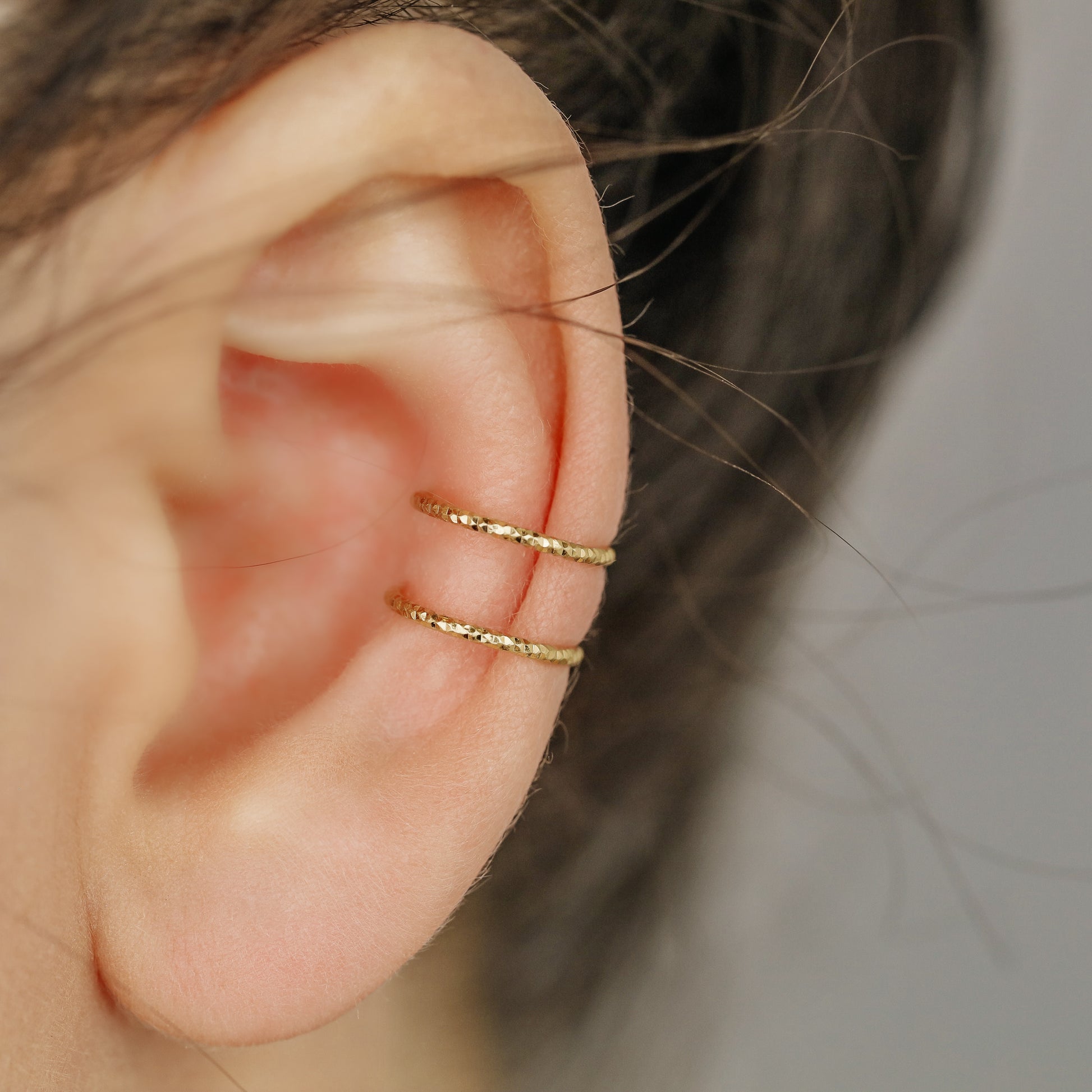 Gold double band ear cuff worn on the upper ear, featuring a slim no piercing design with diamond cut sparkle texture.