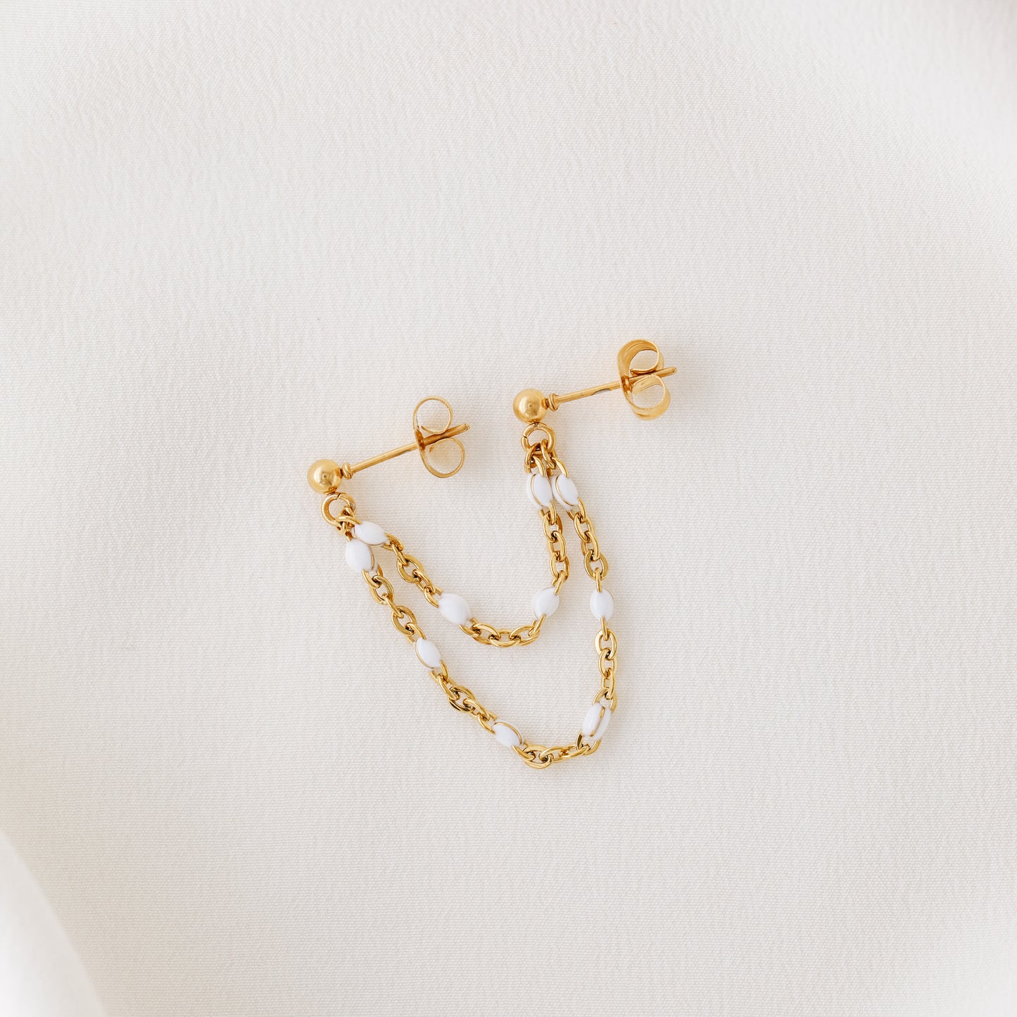 Gold double chain stud earring displayed on white fabric with delicate draped chains