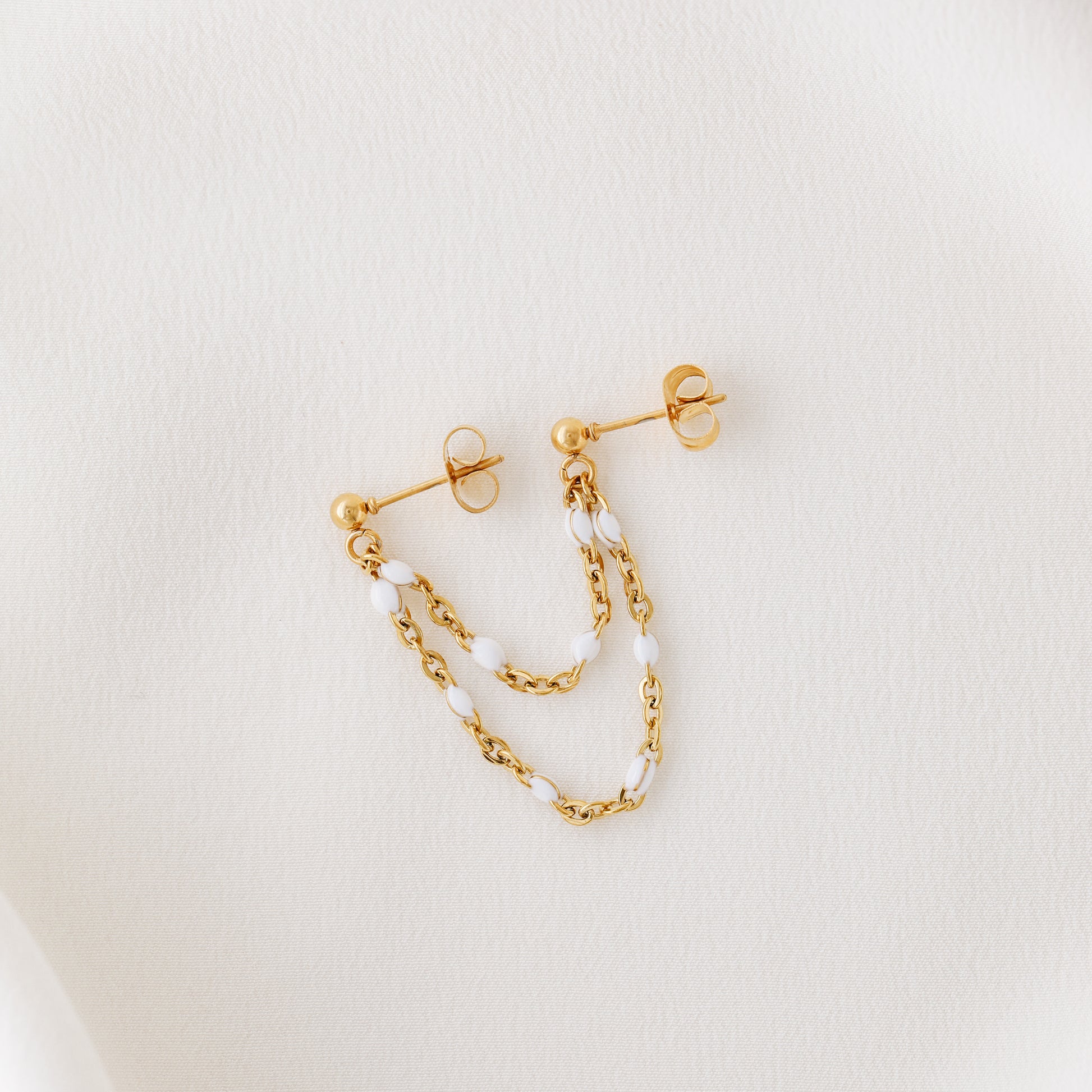 Gold double chain stud earring displayed on white fabric with delicate draped chains