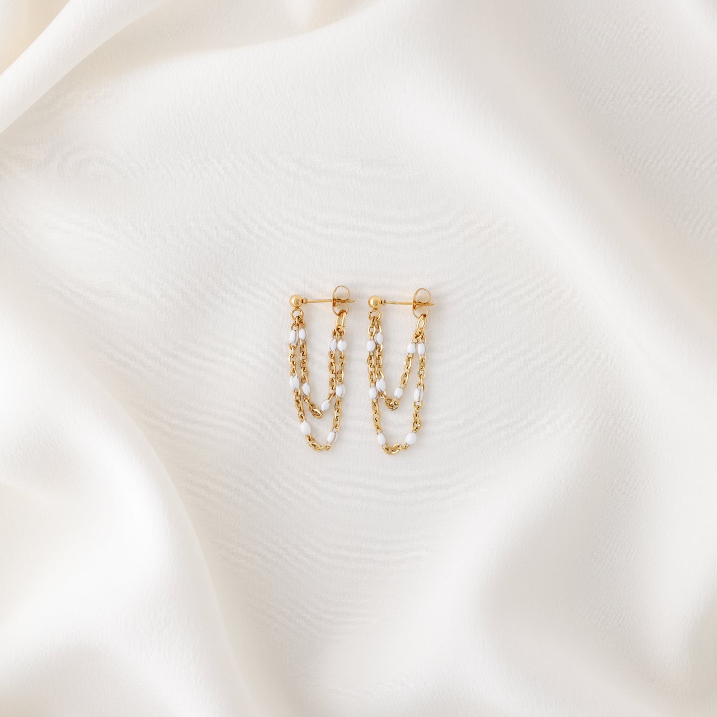 Gold double chain dangle earrings displayed on white fabric with push back closure