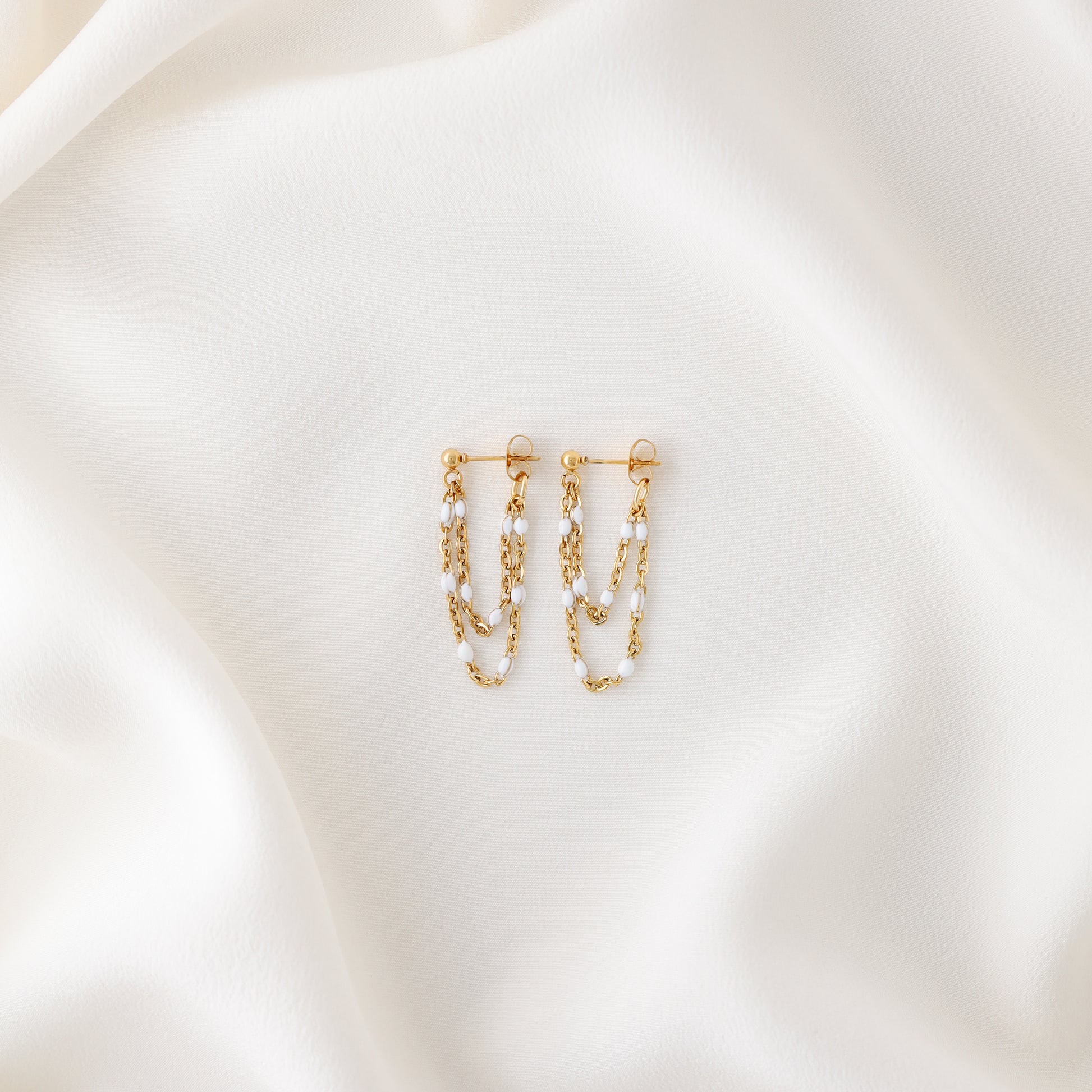 Gold double chain dangle earrings displayed on white fabric with push back closure