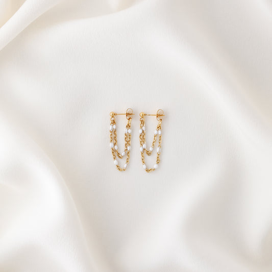 Gold double chain dangle earrings displayed on white fabric with push back closure
