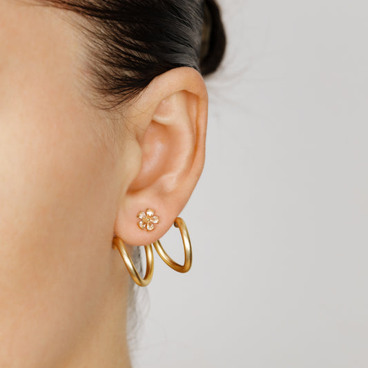 Gold double loop Ear Jacket shown worn in two different orientations behind the earlobe with a small floral stud, demonstrating how the curved design can change position around the ear.