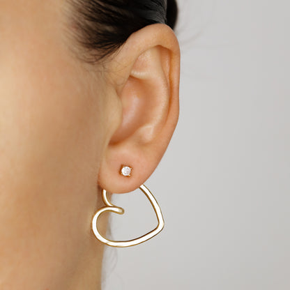 Gold heart Ear Jacket worn behind the earlobe with a small clear crystal stud, showing the open heart silhouette and layered two-part earring effect.