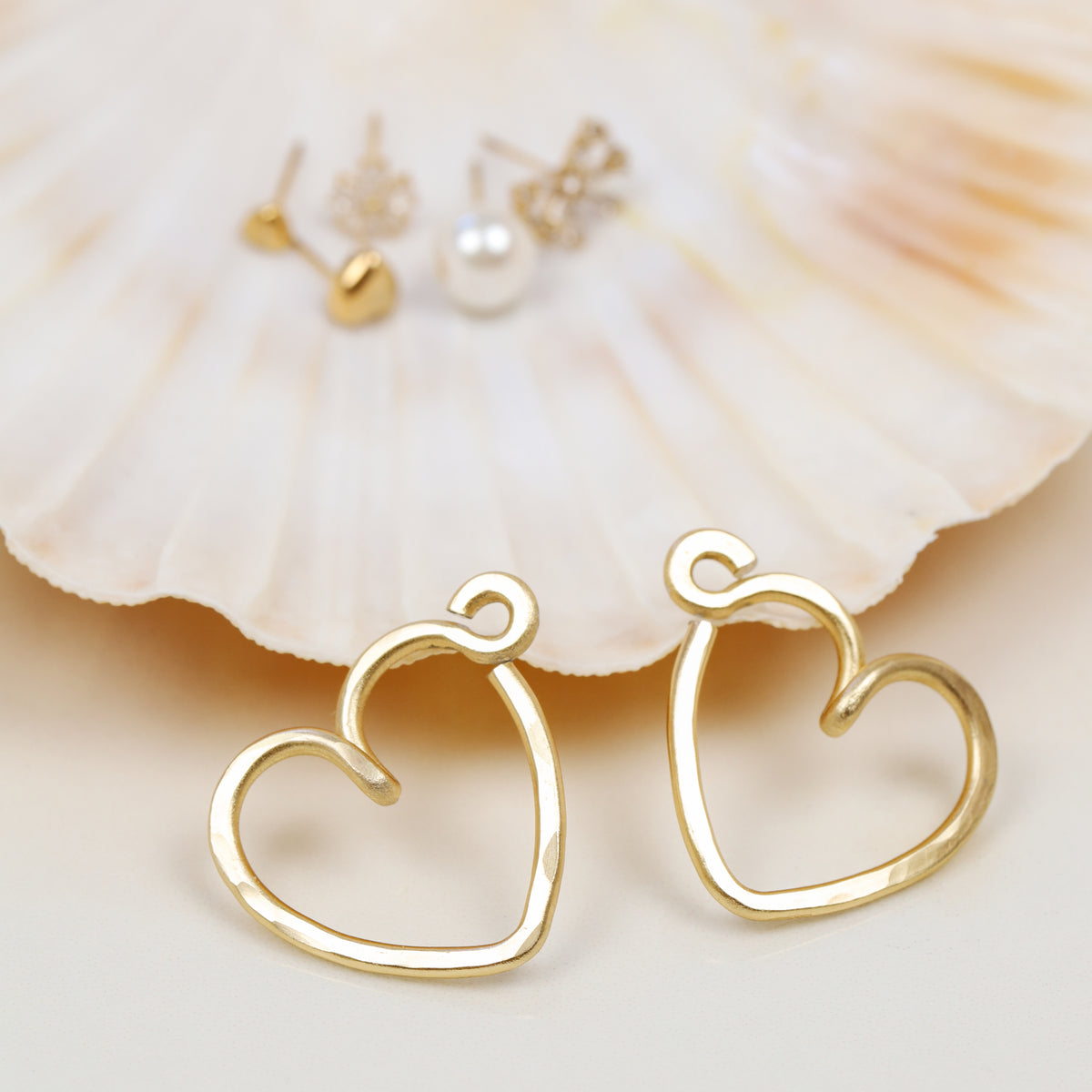 Pair of gold heart Ear Jacket backs displayed beside assorted stud earrings, illustrating how the interchangeable Ear Jacket design can be combined with different compatible studs.