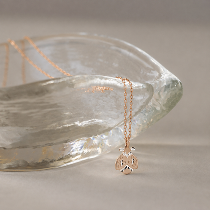 Gold ladybug necklace displayed beside textured glass bowl with soft neutral background