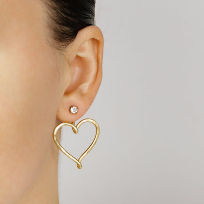 Gold Large Heart Ear Jacket worn behind the pierced earlobe with a small clear crystal stud, showing how the open heart silhouette hangs beneath the lobe.