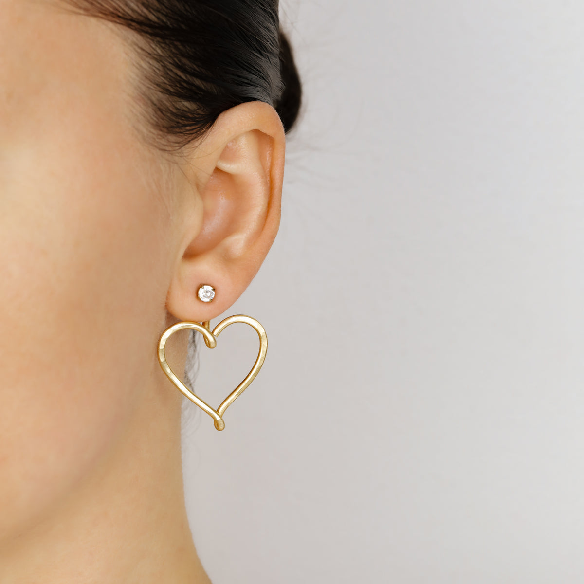 Pair of gold Large Heart Ear Jackets displayed with clear crystal stud earrings, showing the matching pair option and hammered open heart design.