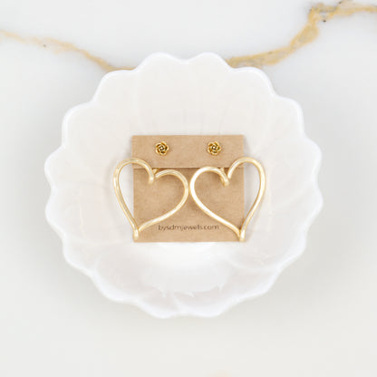 Pair of gold hammered Large Heart Ear Jackets displayed on a jewelry card inside a white dish with small rose-shaped stud earrings as a styling example.