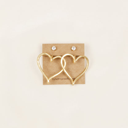 Pair of gold hammered Large Heart Ear Jackets displayed on a jewelry card inside a white dish with small rose-shaped stud earrings as a styling example.