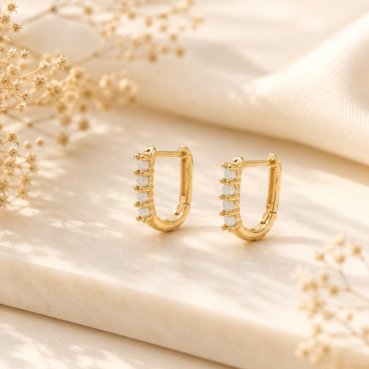 Close up of gold huggie hoop earrings with iridescent opal stones and latch back closure