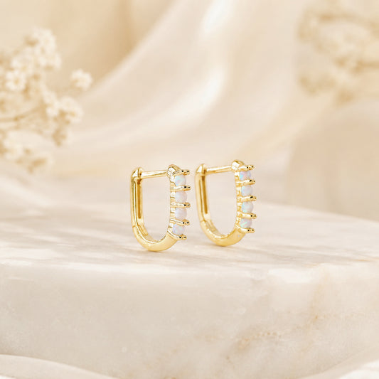 Pair of gold opal huggie earrings displayed on a neutral stone surface