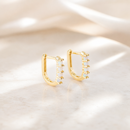 Pair of gold opal huggie earrings displayed on a neutral stone surface