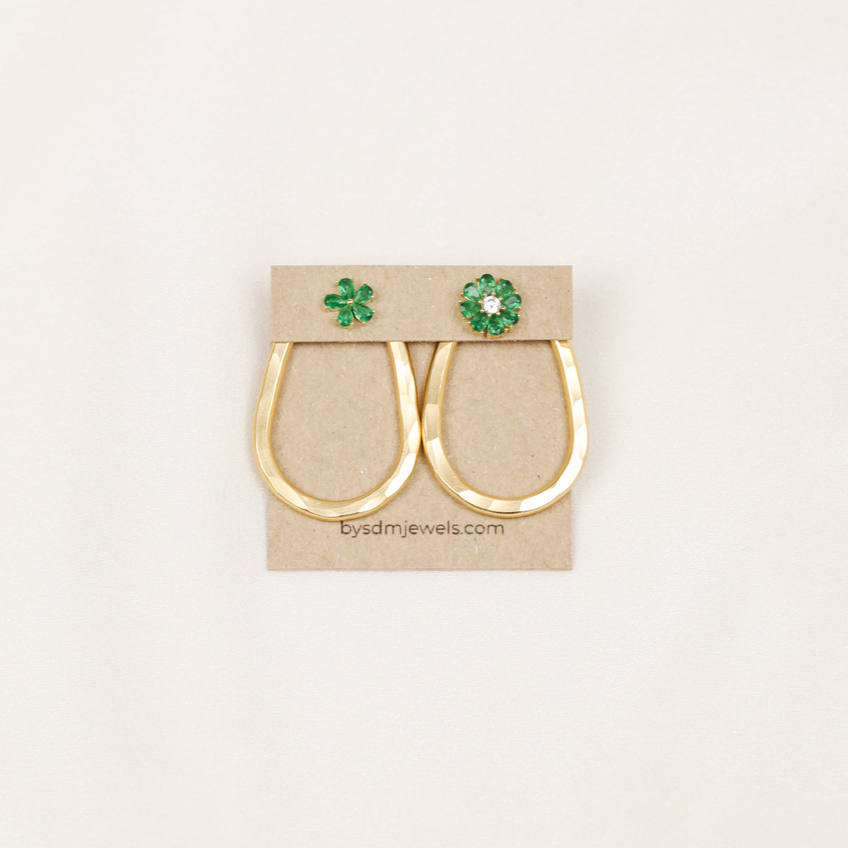 Matching pair of gold hammered teardrop ear jackets displayed with decorative green studs on a jewelry card.