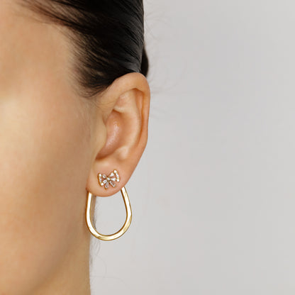 Gold hammered teardrop ear jacket worn behind the earlobe with a decorative stud at the front, showing the open elongated shape suspended below the ear.