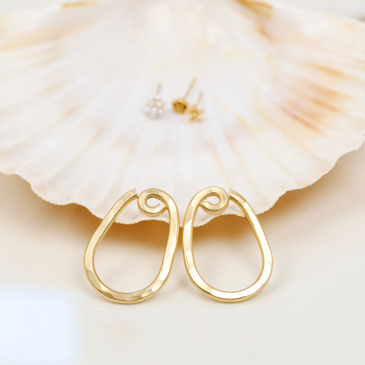 Close-up of a matching pair of gold hammered teardrop ear jacket backs showing the elongated open shape and handmade textured surface.