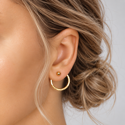 Gold round ear jacket worn behind the earlobe with a small ball stud at the front, showing the hammered circular jacket suspended beneath the ear.