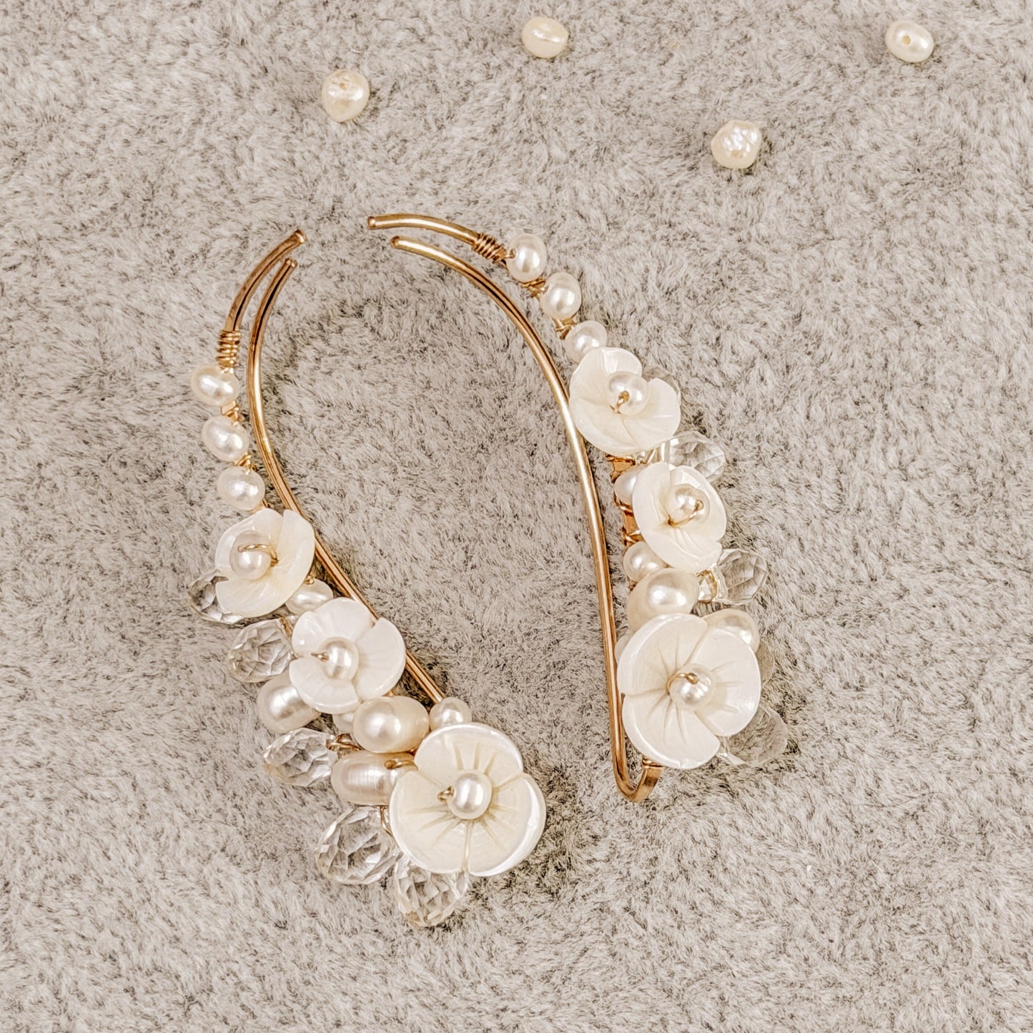 Handmade pearl flower ear climbers displayed on neutral fabric with scattered pearls