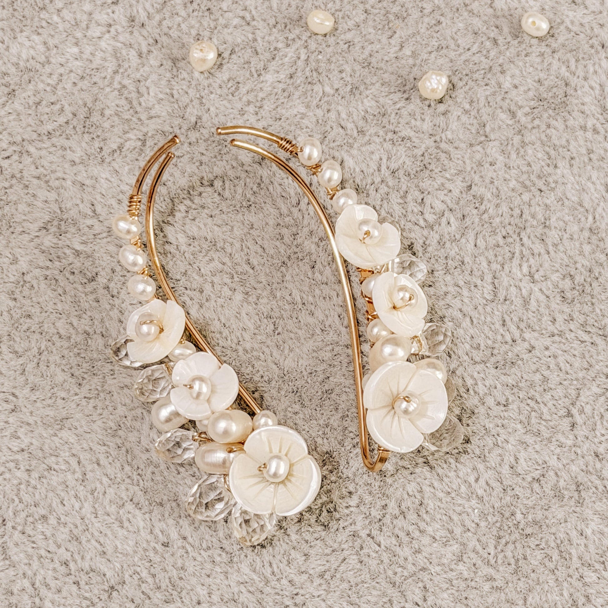 Handmade pearl flower ear climbers displayed on neutral fabric with scattered pearls