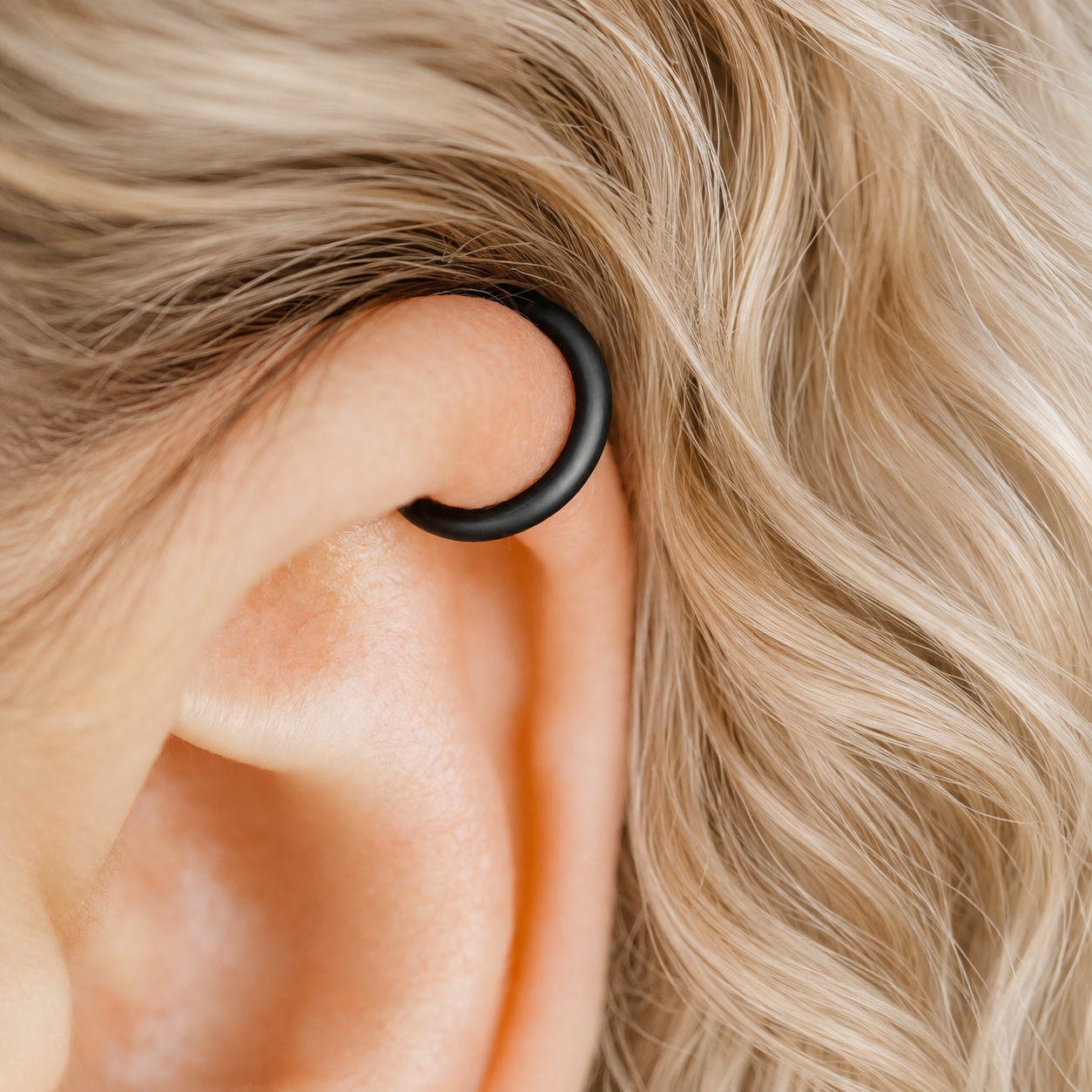 Thick smooth no-piercing ear cuff shown worn on different areas of the ear, including lobe, conch, cartilage and upper helix, with a rounded wrap design available in sterling silver, 18k yellow gold plated sterling silver, 18k rose gold plated sterling silver and black aluminum.