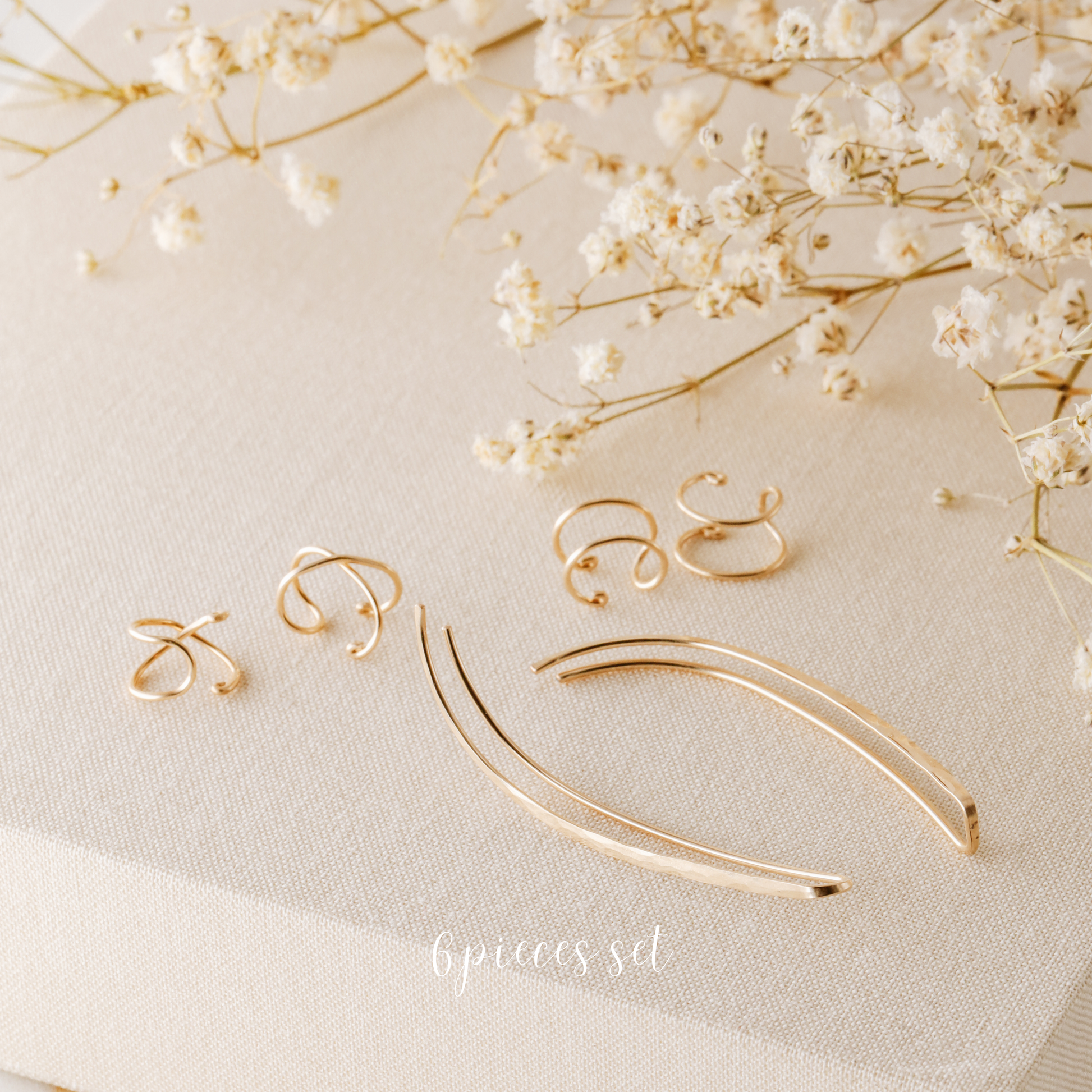 6 pieces ear climber set displayed on beige fabric with dried white flowers, featuring a pair of long hammered ear climbers, two Double Line no-piercing helix cuffs and two Criss-Cross no-piercing helix cuffs in a warm gold finish.