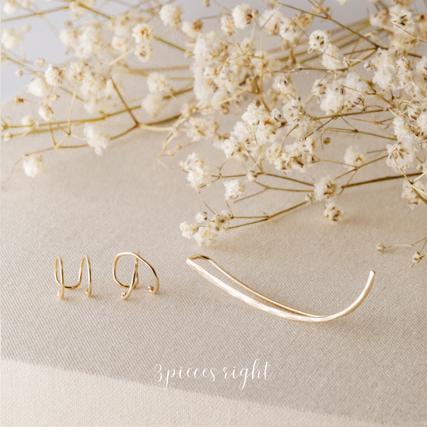 3 pieces right ear climber set displayed on beige fabric with dried white flowers, featuring one long hammered ear climber for the right ear, one Double Line no-piercing helix cuff and one Criss-Cross no-piercing helix cuff in a warm gold finish.