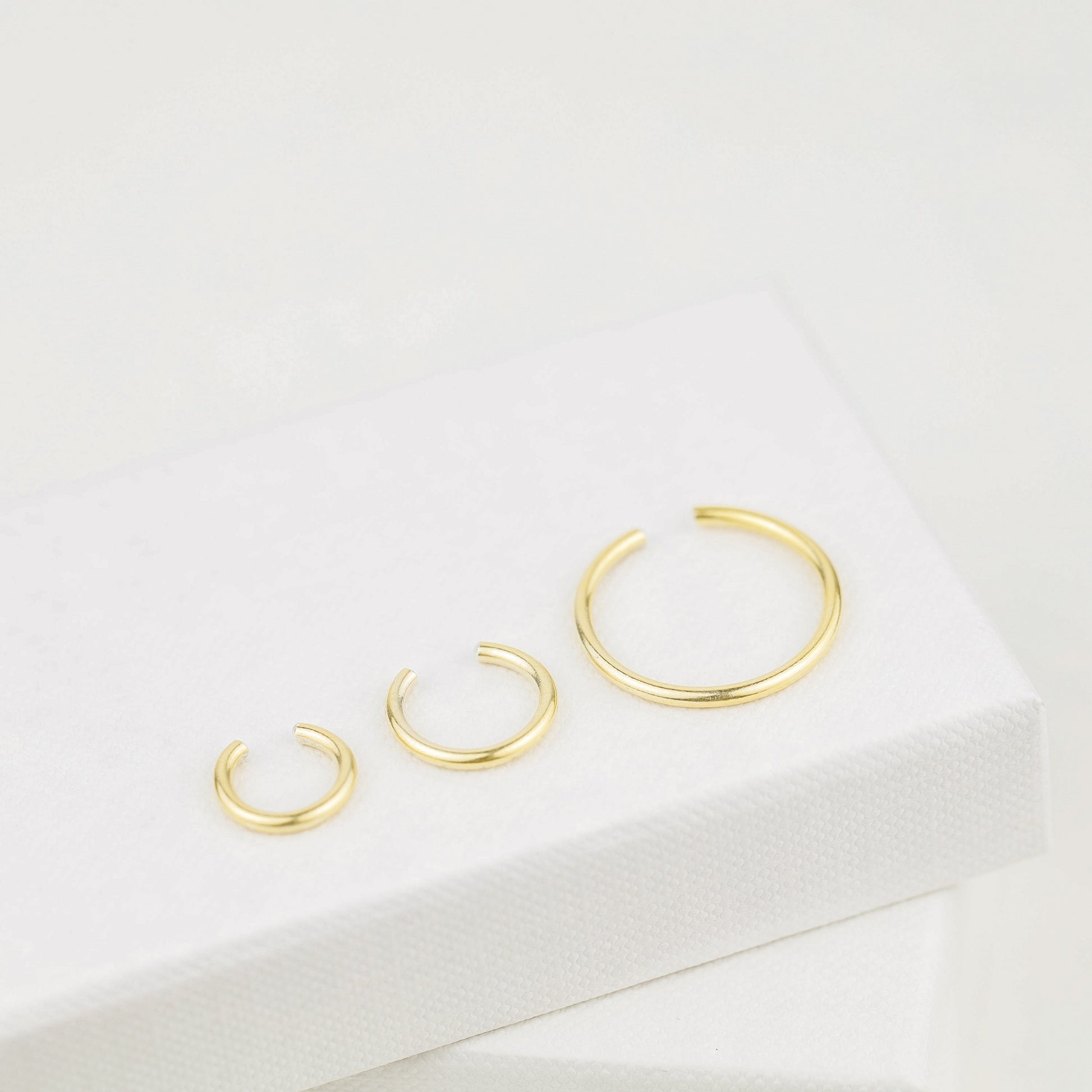 Thick smooth no-piercing ear cuff shown worn on different areas of the ear, including lobe, conch, cartilage and upper helix, with a rounded wrap design available in sterling silver, 18k yellow gold plated sterling silver, 18k rose gold plated sterling silver and black aluminum.
