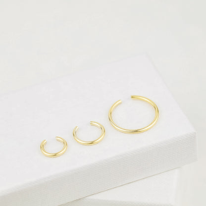 Thick smooth no-piercing ear cuff shown worn on different areas of the ear, including lobe, conch, cartilage and upper helix, with a rounded wrap design available in sterling silver, 18k yellow gold plated sterling silver, 18k rose gold plated sterling silver and black aluminum.
