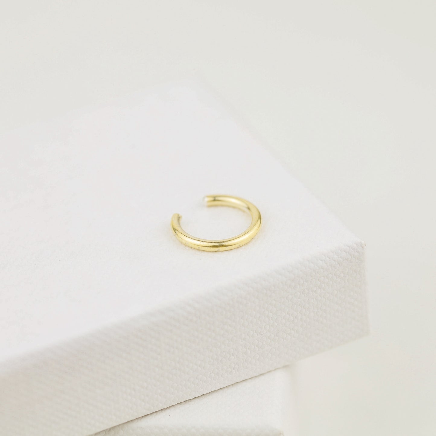 Thick smooth no-piercing ear cuff shown worn on different areas of the ear, including lobe, conch, cartilage and upper helix, with a rounded wrap design available in sterling silver, 18k yellow gold plated sterling silver, 18k rose gold plated sterling silver and black aluminum.