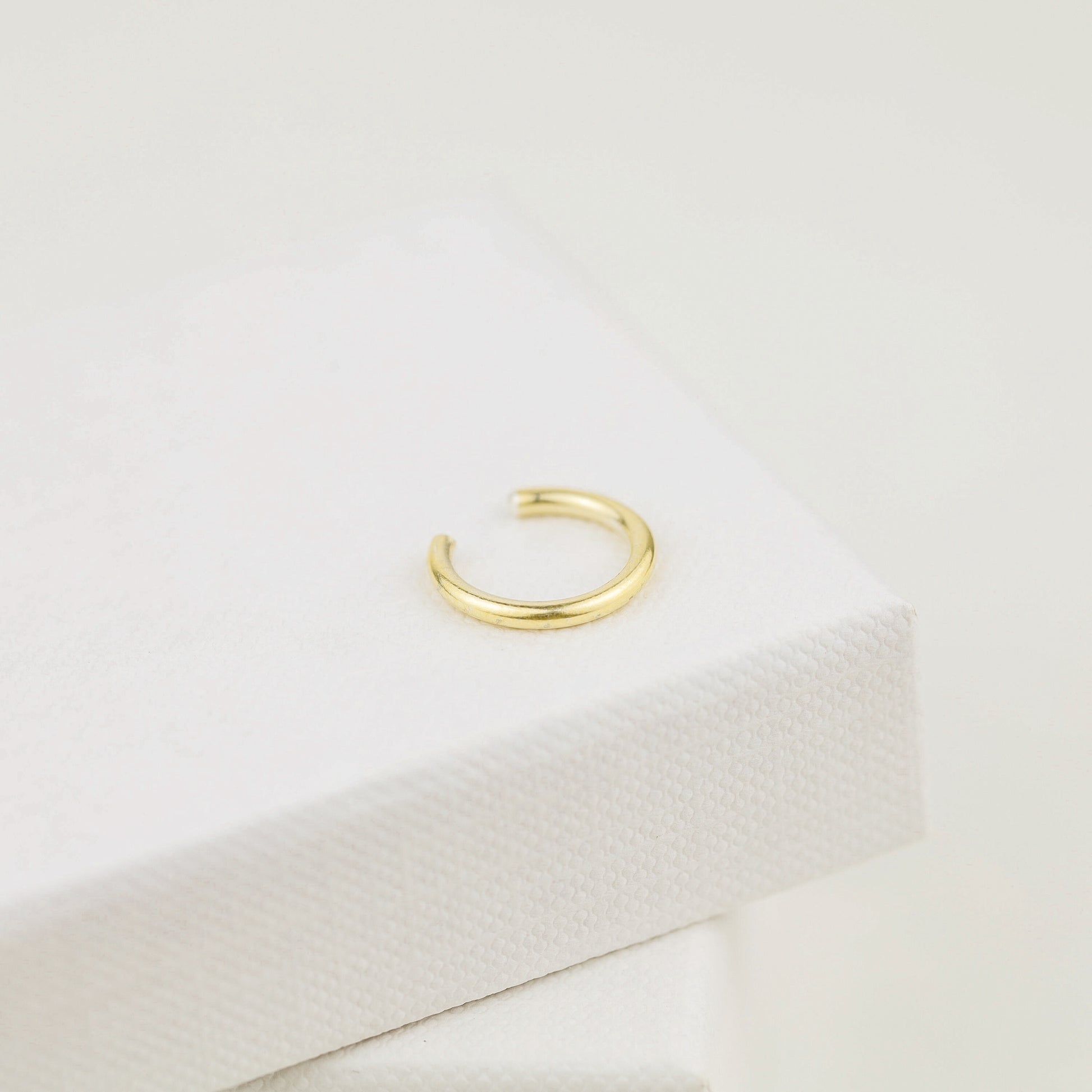 Thick smooth no-piercing ear cuff shown worn on different areas of the ear, including lobe, conch, cartilage and upper helix, with a rounded wrap design available in sterling silver, 18k yellow gold plated sterling silver, 18k rose gold plated sterling silver and black aluminum.