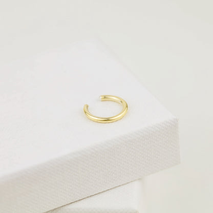 Thick smooth no-piercing ear cuff shown worn on different areas of the ear, including lobe, conch, cartilage and upper helix, with a rounded wrap design available in sterling silver, 18k yellow gold plated sterling silver, 18k rose gold plated sterling silver and black aluminum.