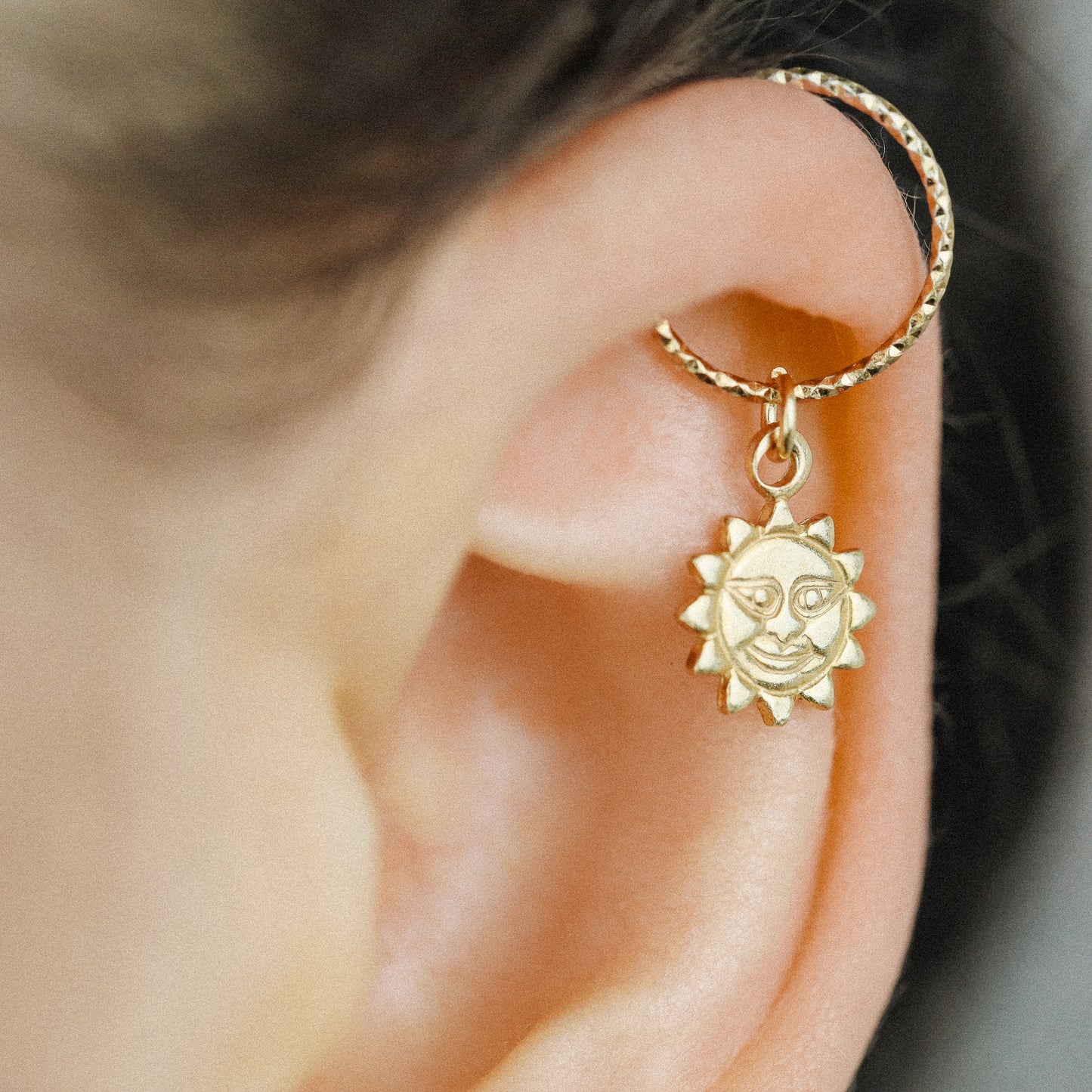 Side view of a gold celestial sun pendant hoop earring on a model's ear showing the seamless twist closure.
