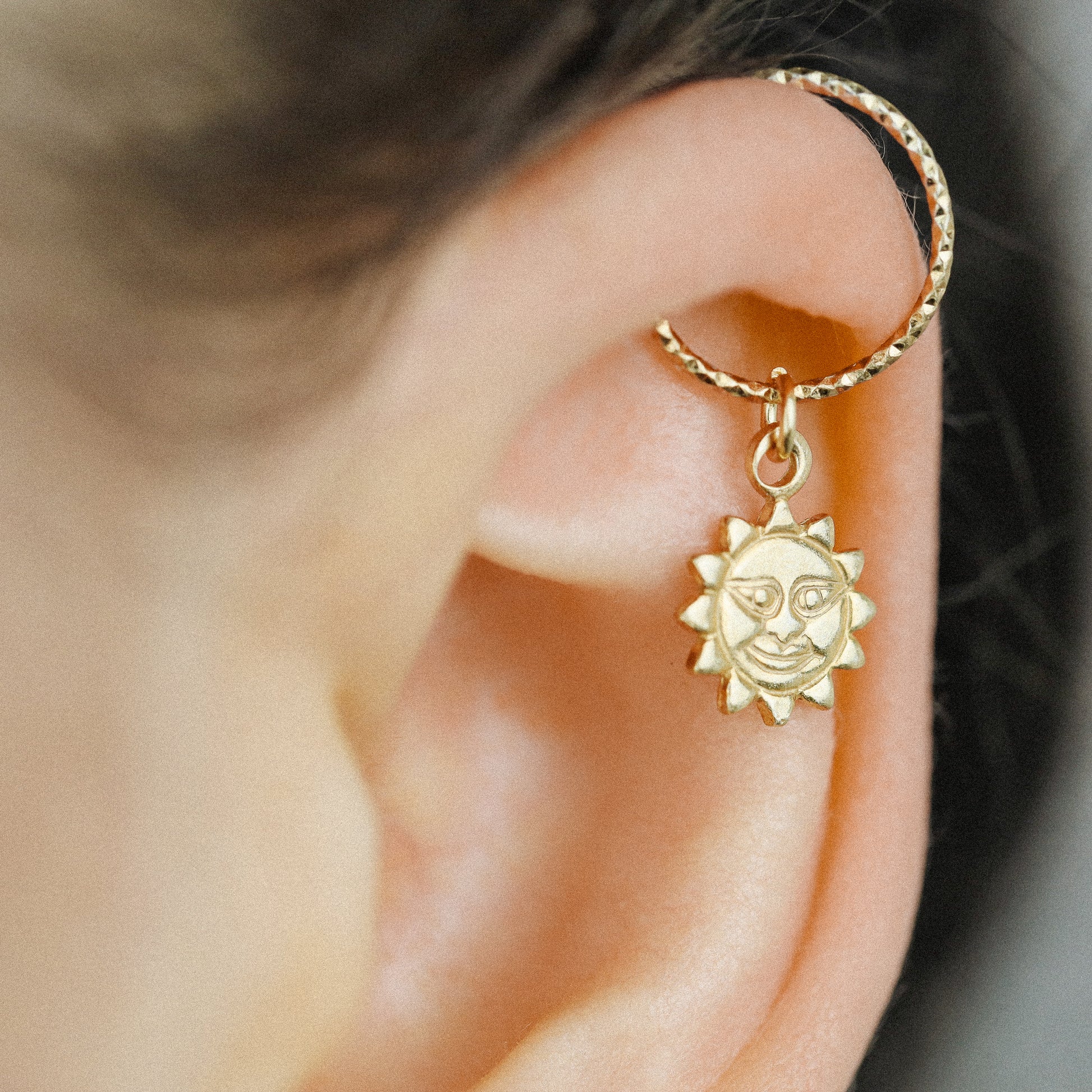 Side view of a gold celestial sun pendant hoop earring on a model's ear showing the seamless twist closure.