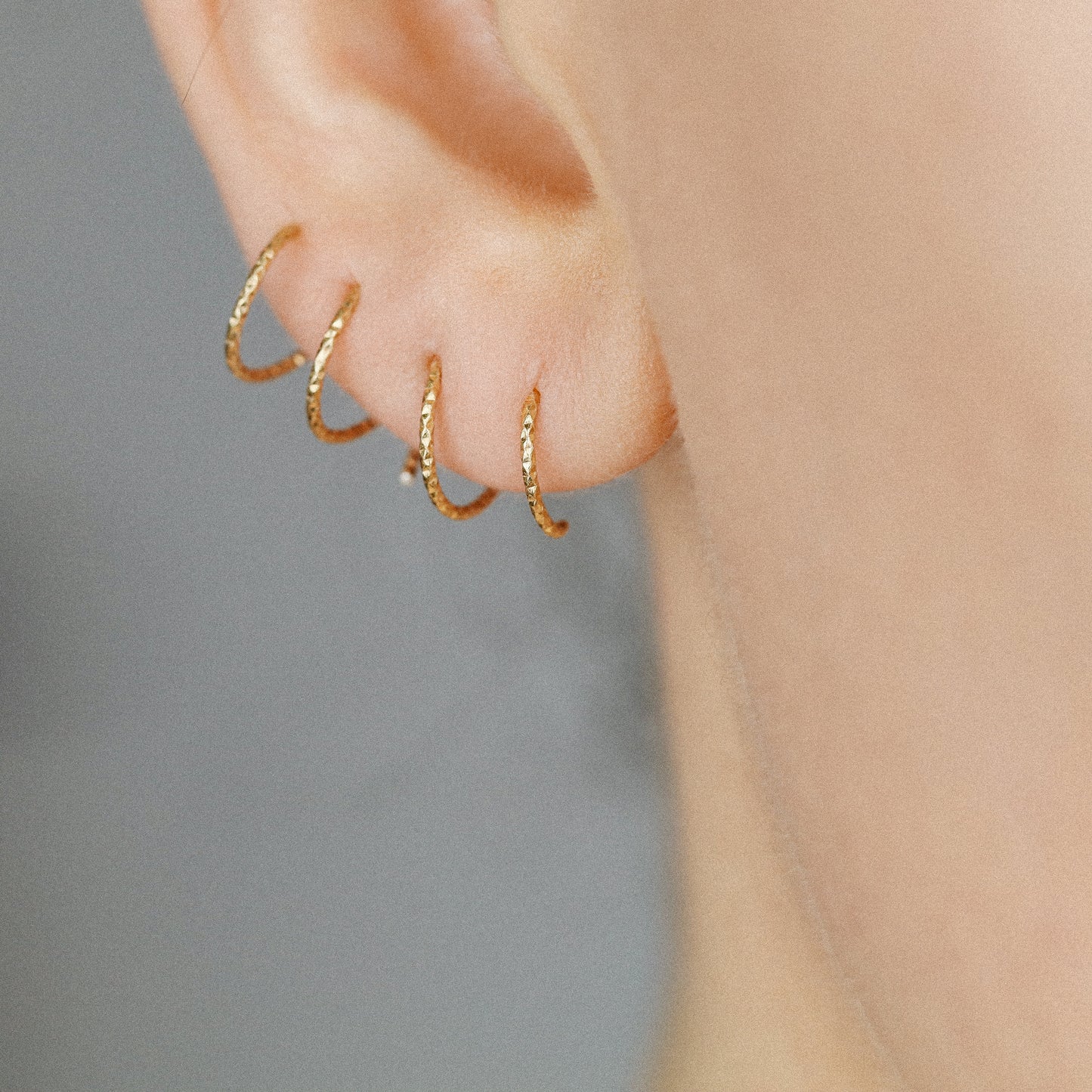 Minimal gold double hoop earrings with spiral twist design worn on ear, illusion of double piercing, diamond cut sterling silver jewelry