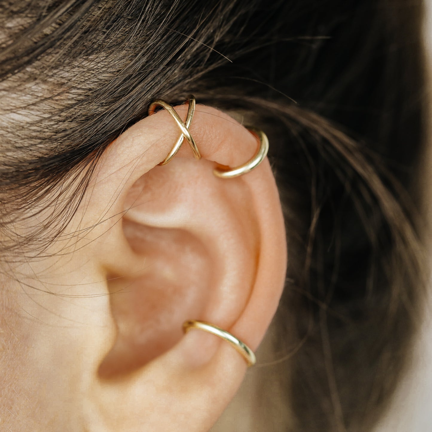 Thick smooth no-piercing ear cuff shown worn on different areas of the ear, including lobe, conch, cartilage and upper helix, with a rounded wrap design available in sterling silver, 18k yellow gold plated sterling silver, 18k rose gold plated sterling silver and black aluminum.